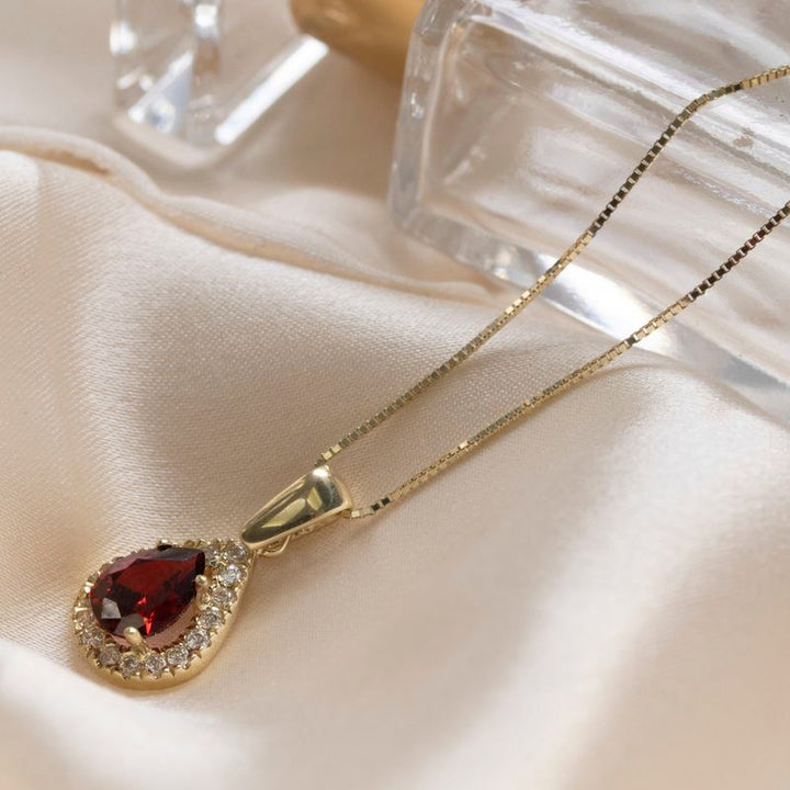 yellow gold drop necklace with white zircons and a garnet stone in the center