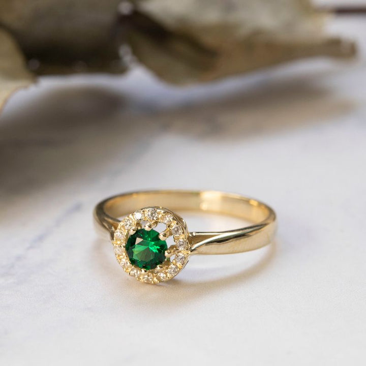 round yellow gold ring with white zircons and a green zircon in the center