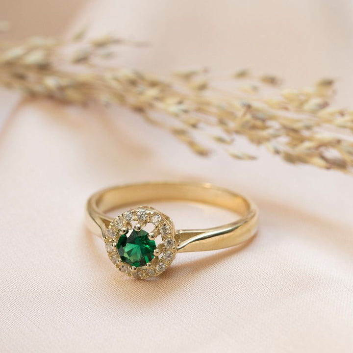 round yellow gold ring with white zircons and a green zircon in the center