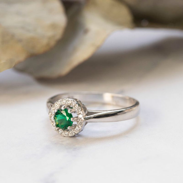 round yellow gold ring with white zircons and a green zircon in the center